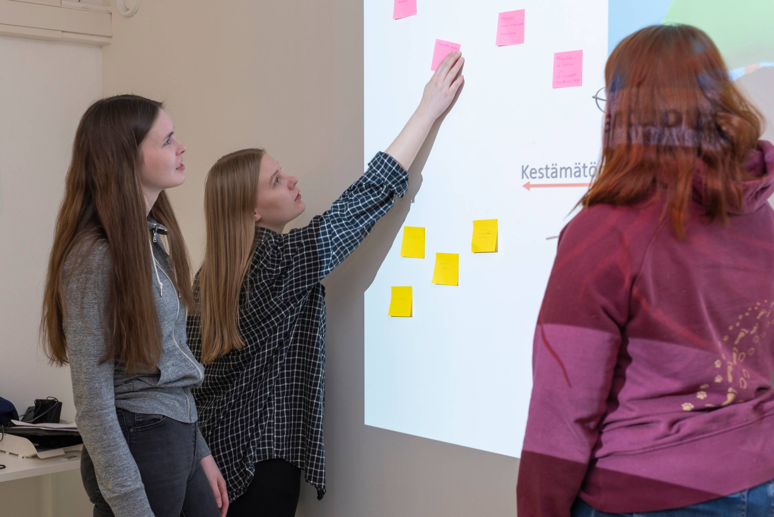 Kolme opiskelijaa tarkastelemassa valkotaululla olevia muistilappuja